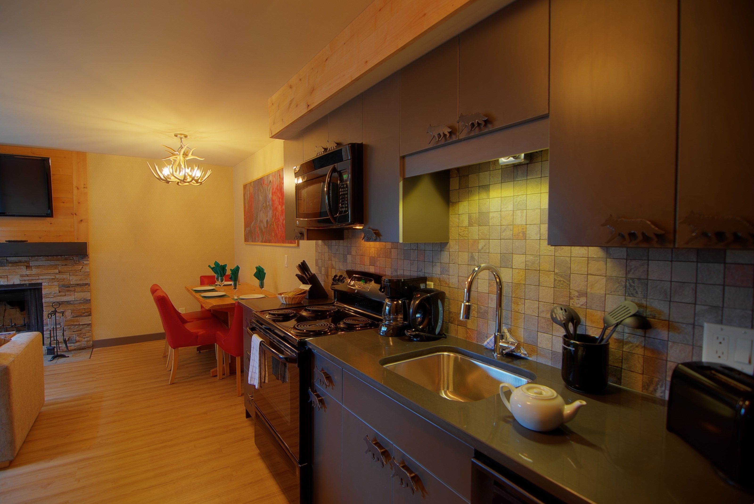 A modern kitchen with a built-in microwave, stove, and sink. There is a dining area with a red chair and a table.