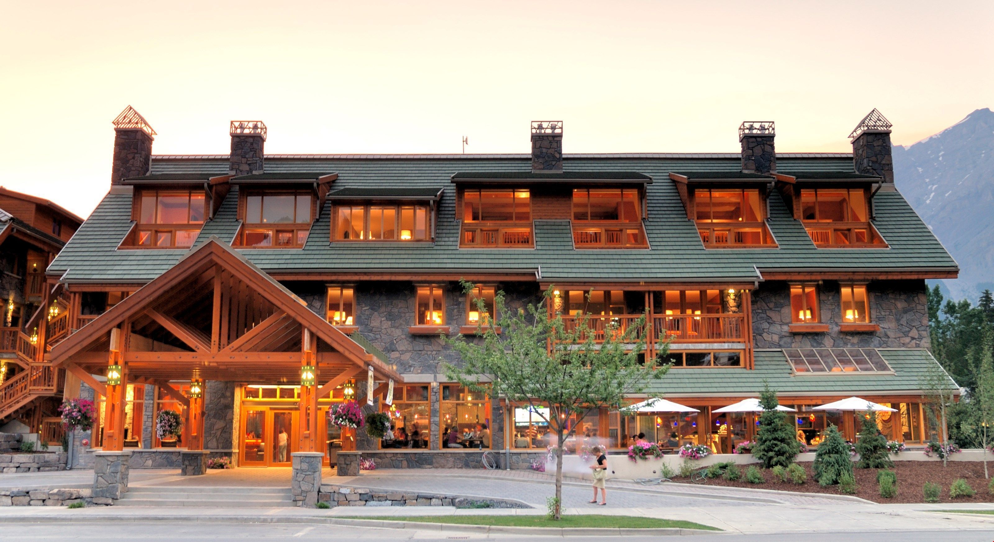 Un grand chalet à étages, doté d’une façade en pierre, de balcons en bois et d’une entrée imposante surmontée d’un porche abrité.