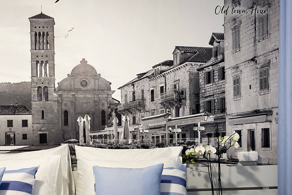 Cama com roupa de cama e toalhas listradas, uma orquídea em vaso, e vista para edifícios históricos incluindo o topo de uma igreja.