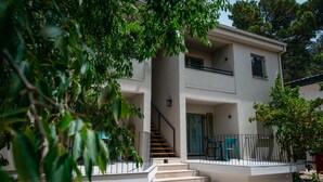 A two-story building with a staircase leading to the entrance, surrounded by greenery. - Family Resort Urania (Baska Voda)