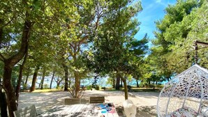 An outdoor seating area with a table and chairs, surrounded by trees and a hanging chair. - Family Resort Urania (Baska Voda)