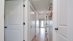 A hallway with white doors, a patterned curtain, and a ceiling light fixture. - Ocean View Retreat! Pets, Fenced, Community Pool (Galveston)