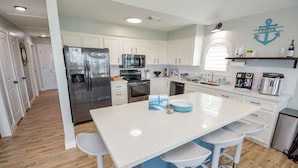A modern kitchen with white cabinets, stainless steel appliances, and a central island with bar stools. - Ocean View Retreat! Pets, Fenced, Community Pool (Galveston)