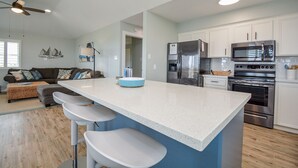 A modern kitchen with white cabinets, stainless steel appliances, and a central island with bar stools. - Ocean View Retreat! Pets, Fenced, Community Pool (Galveston)
