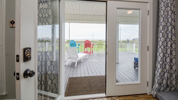 A door leading to an outdoor deck with a view of a fenced area and chairs. - Ocean View Retreat! Pets, Fenced, Community Pool (Galveston)