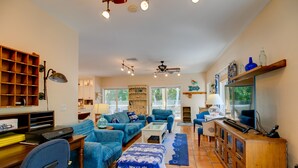 A spacious living room with a blue sofa set, a wooden cabinet, and a television. - Whimsea: West End, Pets OK, Pool Home on Canal! (Sanibel)
