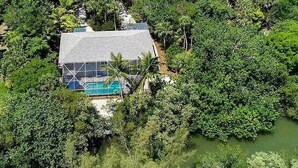 An aerial view of a house surrounded by dense greenery and a small body of water. - Whimsea: West End, Pets OK, Pool Home on Canal! (Sanibel)