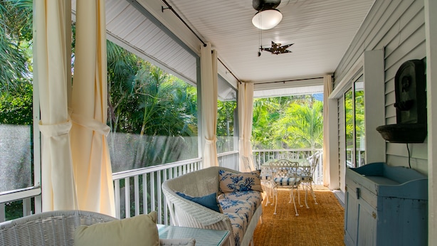 A covered porch with wicker furniture, a cushioned bench, and a dining table. - Whimsea: West End, Pets OK, Pool Home on Canal! (Sanibel)