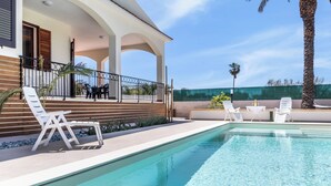 Un área de piscina con sillones de descanso, una pérgola y vistas a la piscina.