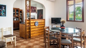 Un comedor con una mesa redonda, sillas, un televisor y vistas a zonas verdes a través de una ventana.