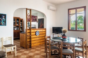 Un comedor con una mesa redonda, sillas, un televisor y vistas a zonas verdes a través de una ventana.