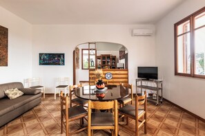 Un salon avec une table ronde, des chaises, un canapé, un téléviseur et une grande fenêtre.