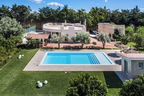 Une piscine entourée d’une pelouse bien entretenue, d’un petit bâtiment et d’une zone délimitée par une clôture, où se trouvent des arbres.