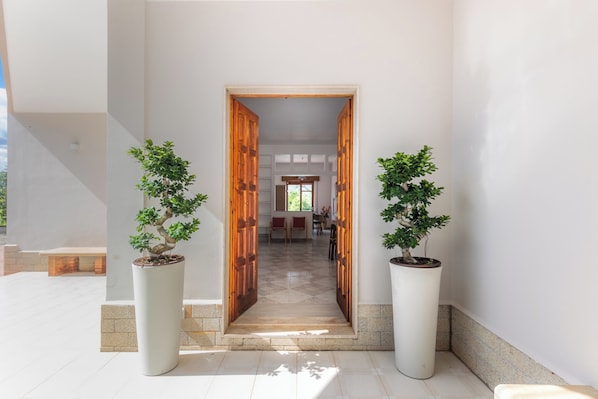 A hallway with a wooden door, potted plants, and a tiled floor.