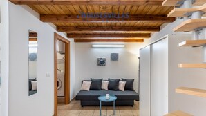 A modern living room with a dark grey sofa, a blue coffee table, and wooden beams on the ceiling. - Iblea House - One Bedroom Apartment, Sleeps 4 (Avola)