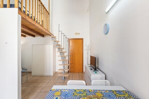 A modern interior with a wooden staircase, a white door, and a television on a white stand.