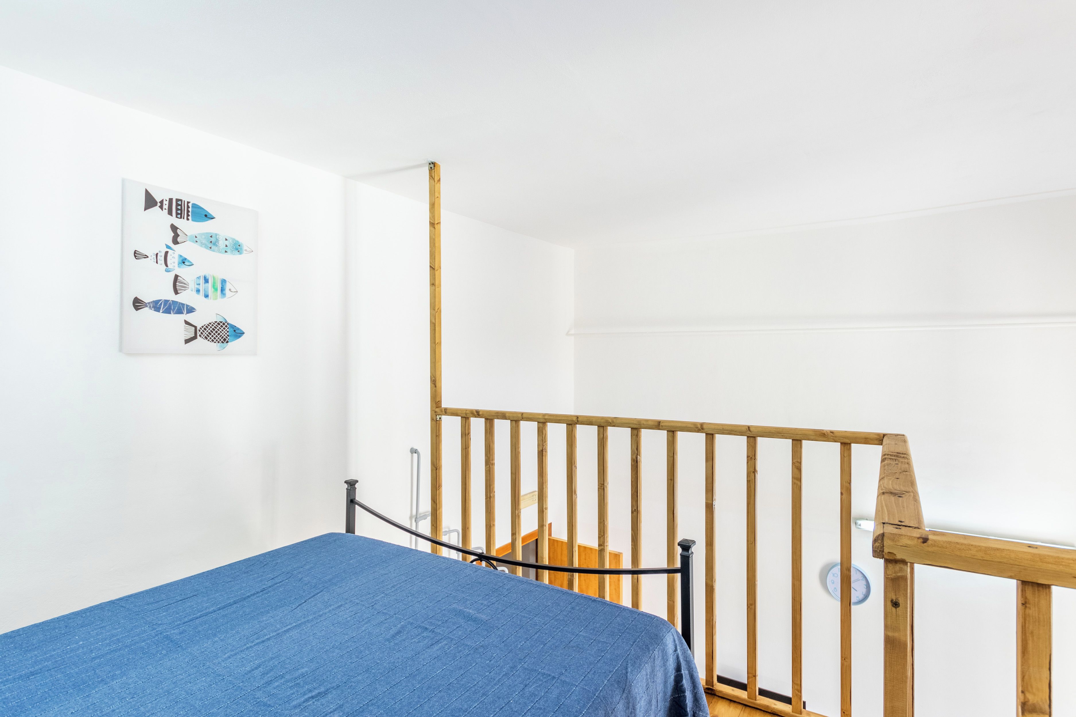 Une chambre à coucher avec un lit, une balustrade en bois, une horloge murale et une œuvre d’art sur le thème des poissons.