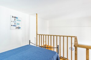 A bedroom with a bed, a wooden railing, a wall-mounted clock, and a fish-themed artwork.