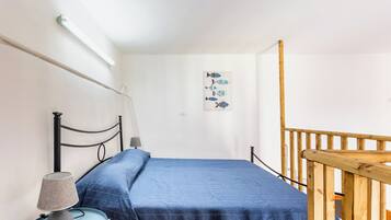Ein Schlafzimmer mit einem Einzelbett, einem Nachttisch mit Lampe, einer Wandleuchte und einem Holzbalken.