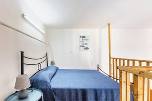 Ein Schlafzimmer mit einem Einzelbett, einem Nachttisch mit Lampe, einer Wandleuchte und einem Holzbalken.