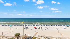 A beach with rows of sun umbrellas and beach chairs, a lifeguard tower, and a clear view of the ocean. - Seaside Serenity Sunbird 503W-Gorgeous Beach Views! Comp Beach Service! (Panama City Beach)