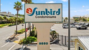 A sign for Sunbird Condominiums with a clear view of a parking lot and a road. - Seaside Serenity Sunbird 503W-Gorgeous Beach Views! Comp Beach Service! (Panama City Beach)
