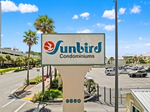 En skylt för Sunbird Condominiums med fri sikt över en parkeringsplats och en väg.