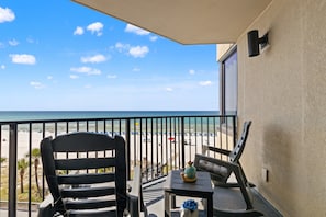 Un balcon avec vue sur la plage, une chaise, une petite table et un objet décoratif.