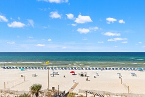 Une plage bordée de rangées de transats et de parasols, une étendue de sable et l’océan.