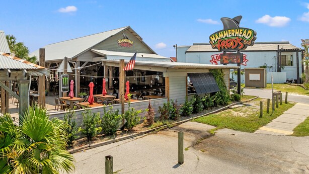 A restaurant with outdoor seating, an American flag, and a distinctive shark-shaped sign. - Seaside Serenity Sunbird 503W-Gorgeous Beach Views! Comp Beach Service! (Panama City Beach)