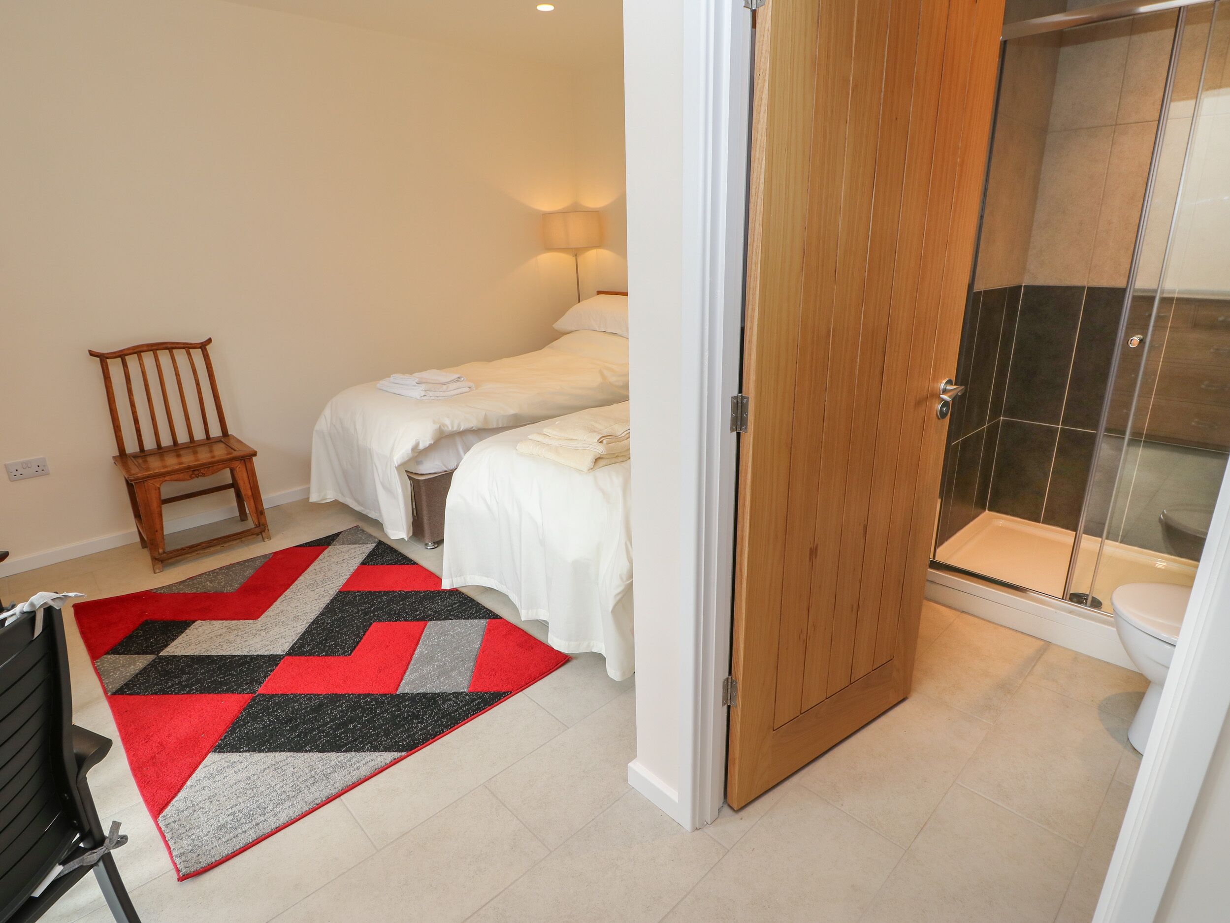 A hotel room with two beds, a shower, and a wooden chair.