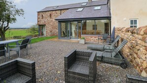 A stone house with a patio area featuring wicker furniture and a view of the countryside.