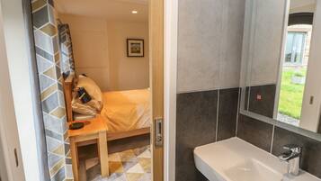 Ein Hotelzimmer mit Bett, Nachttisch aus Holz, Bad mit Waschbecken und Spiegel sowie Blick ins Freie.