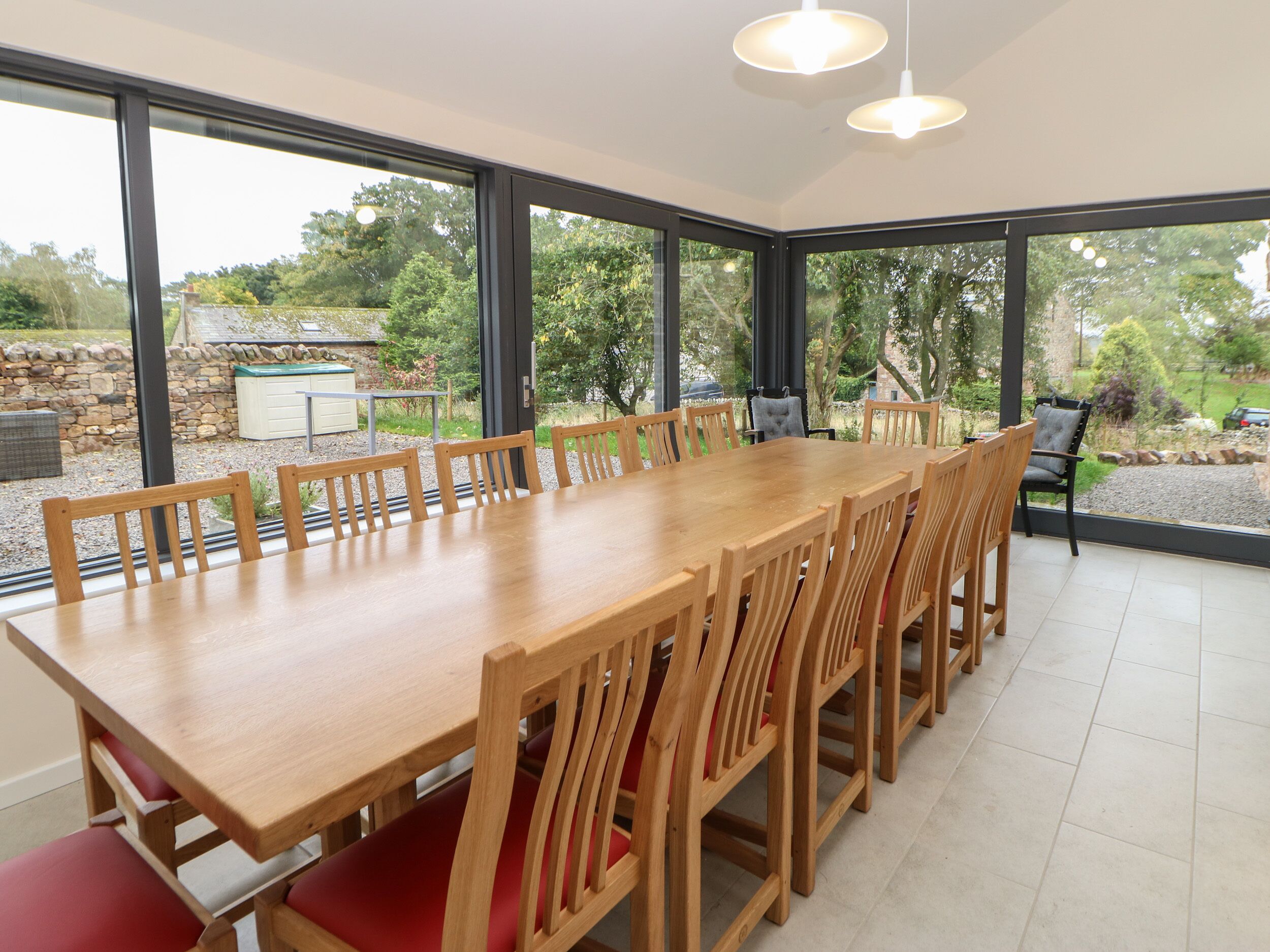 Un comedor con una mesa de madera larga y sillas, ventanas grandes que ofrecen vistas al exterior, y una pared de piedra al fondo.
