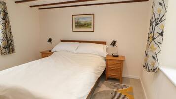 A bedroom with a large bed, wooden headboard, two bedside tables with lamps, a framed picture on the wall, and patterned curtains.