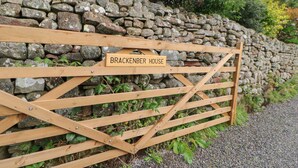 A wooden gate with a sign that reads "Brackenber House" against a stone wall.