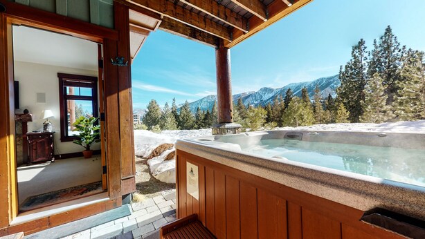 Une terrasse en bois avec un jacuzzi donnant sur un paysage montagneux enneigé.