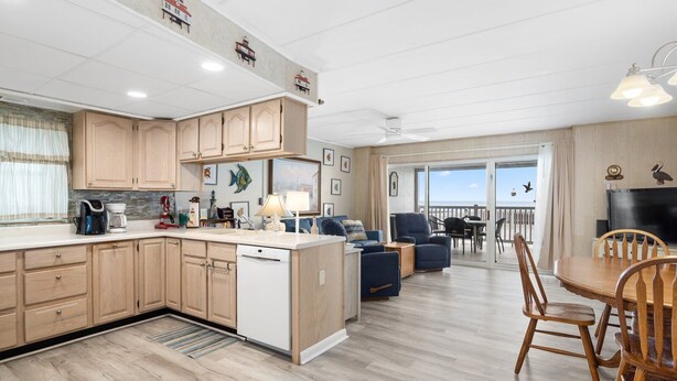 A modern kitchen with wooden cabinets, a dishwasher, and a dining area with a table and chairs. - 3 br / 2 bath for 10, direct beach/ocean and boardwalk views~ (Ocean City)