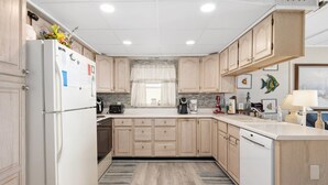 A modern kitchen with wooden cabinets, a refrigerator, a coffee maker, and a window with a view. - 3 br / 2 bath for 10, direct beach/ocean and boardwalk views~ (Ocean City)