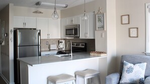 A modern kitchen with white cabinets, stainless steel appliances, a central island with stools, and pendant lighting.