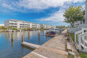 A marina with boats docked, a wooden pier, and a row of apartment buildings.