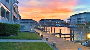 A waterfront hotel with a dock, a row of buildings, and a sunset sky.