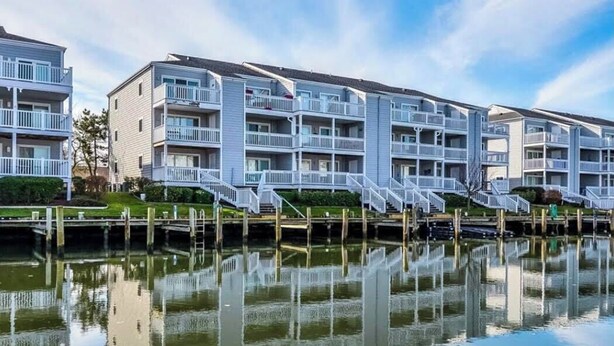 A waterfront residential building with multiple balconies and a reflection in the water.