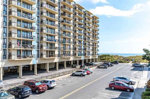 A multi-story hotel with balconies, a parking lot, and a view of the ocean.
