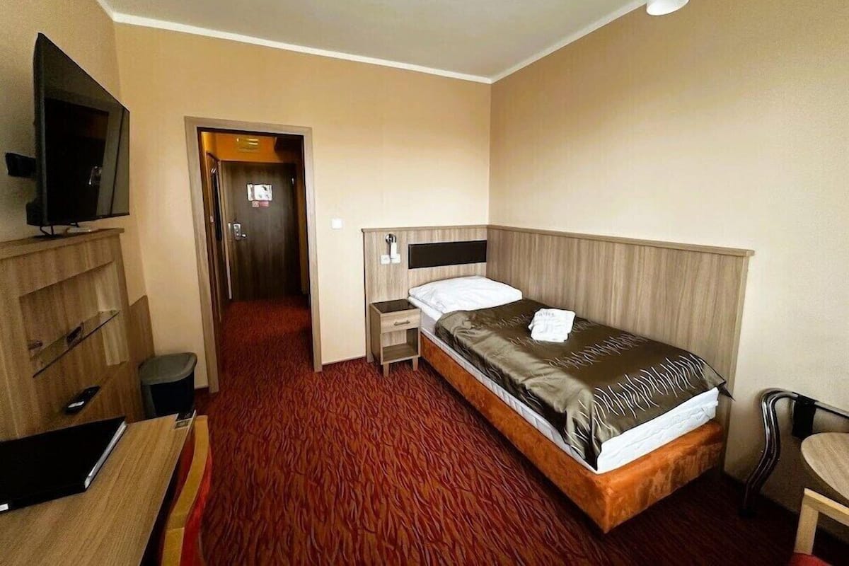 A hotel room with a bed, a desk, a chair, a television, and a door leading to a hallway.