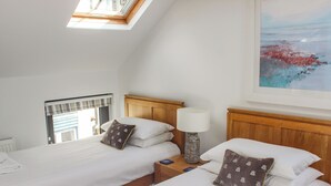 A hotel room with two beds, a skylight, a painting, and a window with a view.