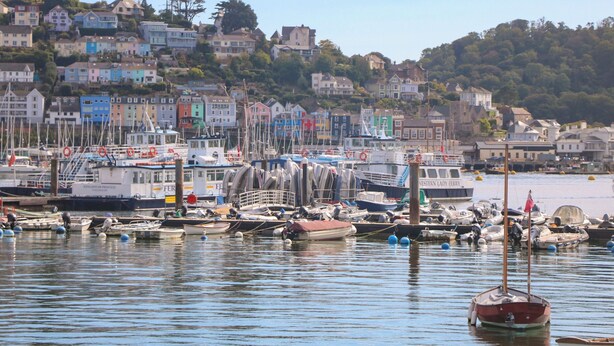 A harbor with various boats docked, a waterfront view, and colorful buildings in the background.