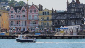 A waterfront with colorful buildings, a dock, and a boat named 'PILOT 4'.
