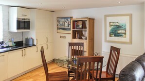 A modern kitchen with white cabinets, a built-in oven, and a dining area with a glass table and wooden chairs.