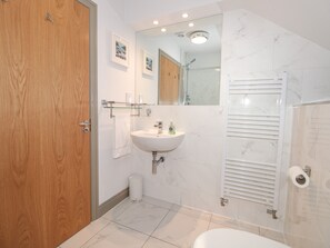 A modern bathroom with a wooden door, a white sink, a mirror, and a shower area. - 6 The Sail Loft (Dartmouth)